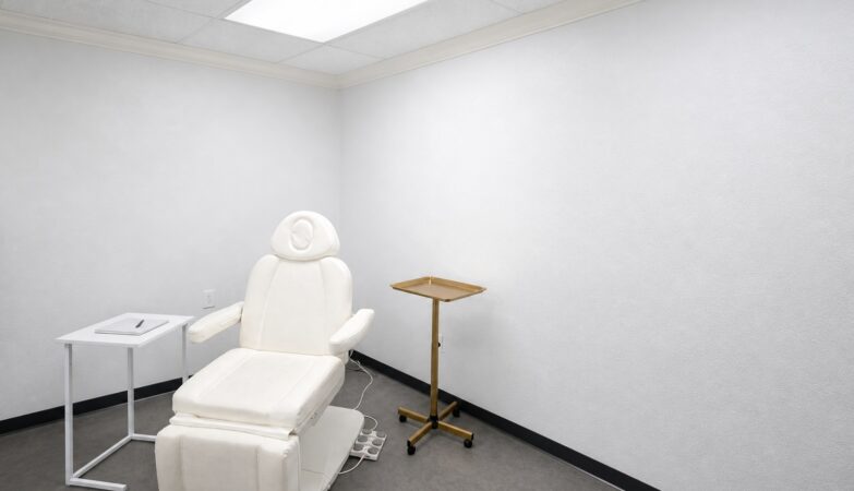 An empty, bright consultation room with a cream treatment chair, a brass tray stand, and a blank notebook on a side table